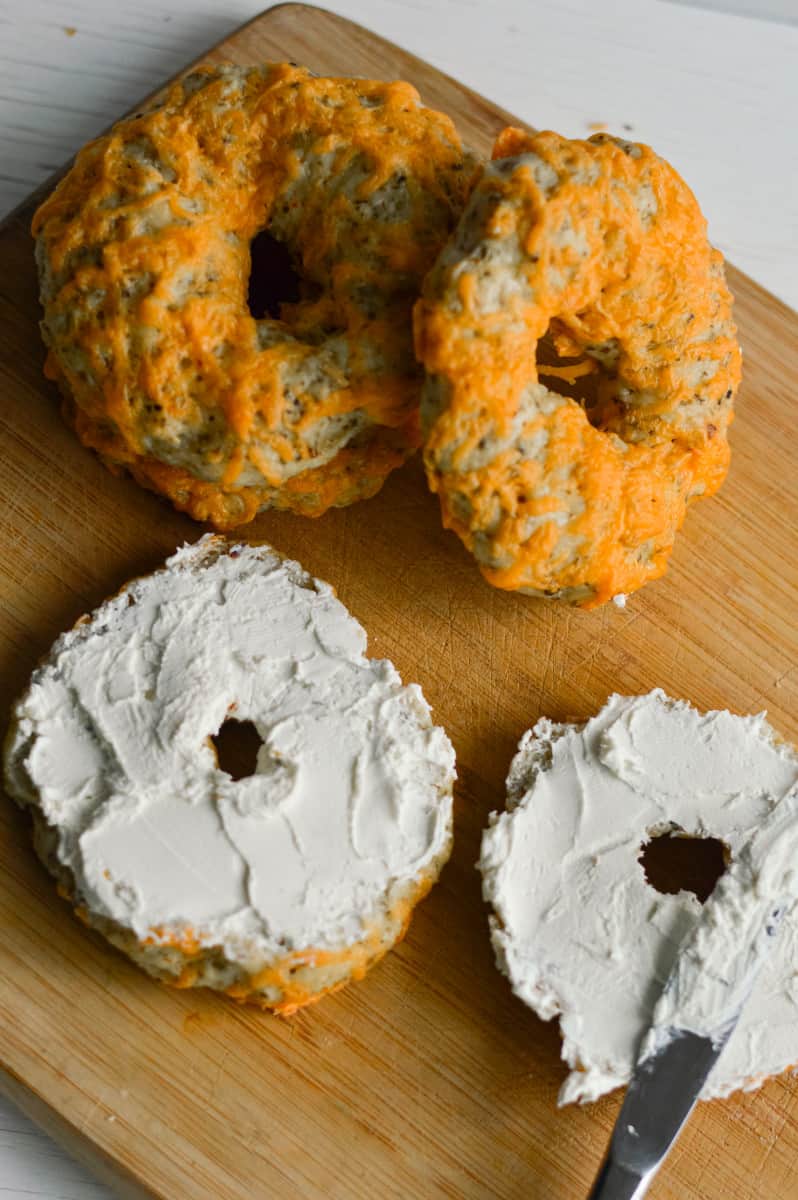 Spreading cream cheese on herb and cheddar bagels.