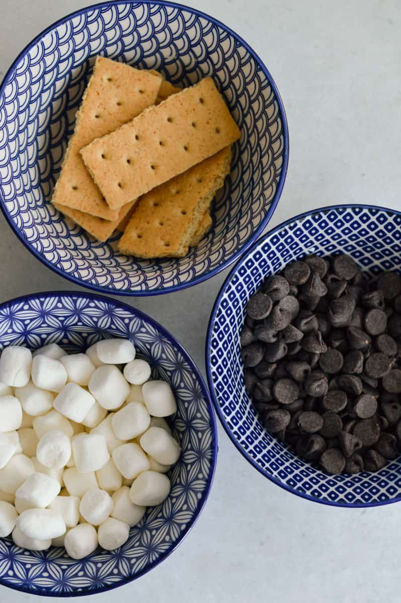 Three bowls with graham crackers, chocolate chips, and marshmallows.