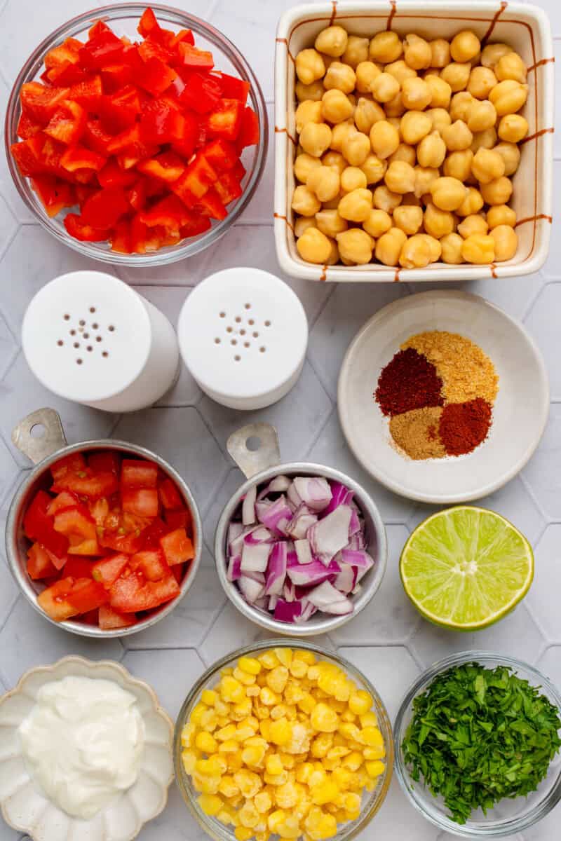 Ingredients for the chickpea salad including chickpeas, red onion, red bell pepper, tomatoes, lime, spices, parsley, corn, and Greek yogurt.