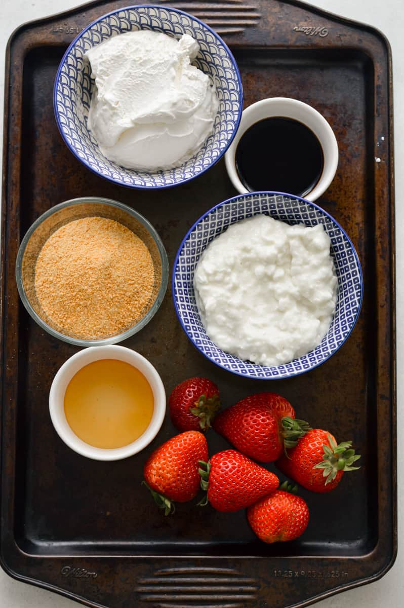 Ingredients including cottage cheese, cool whip, graham crackers, strawberries, vanilla and honey.