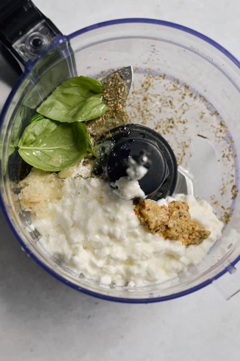 Adding cottage cheese, herbs, lemon juice, garlic and mustard to a food processor.
