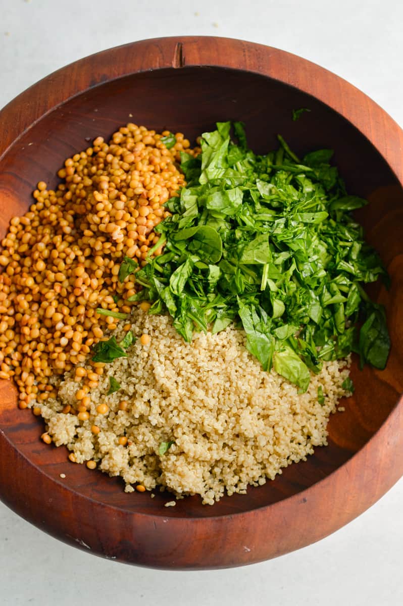 Adding lentils, quinoa and parsley to a mixing bowl.