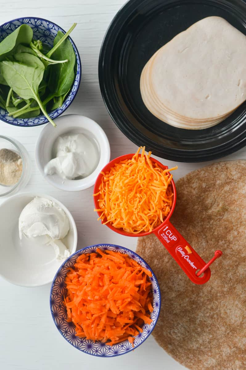Ingredients for roll ups including tortilla, carrots, cheese, turkey and spinach.