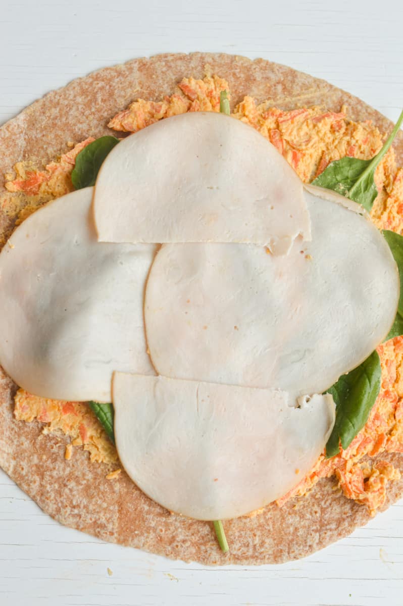 Layering turkey and spinach on tortilla.