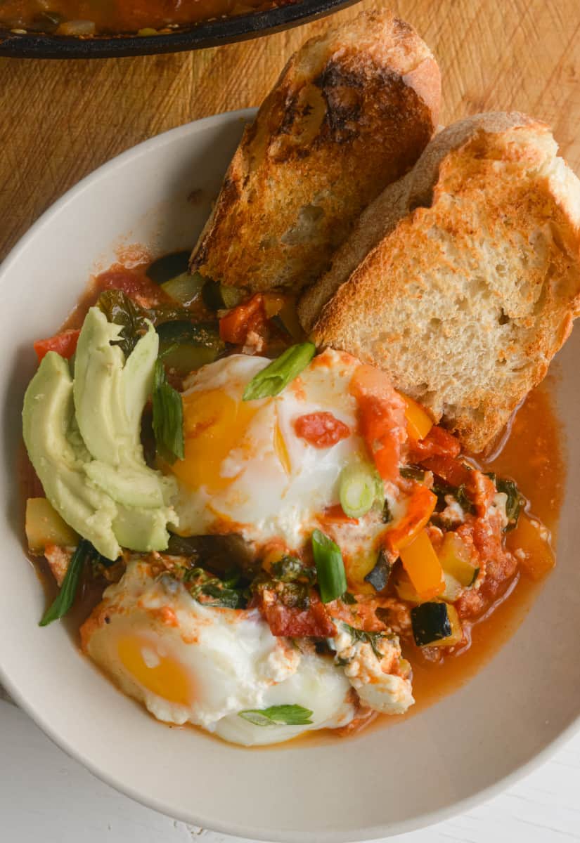 Moroccan shakshuka in a bowl, served with avocado and toast.