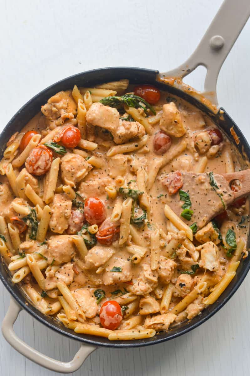Creamy chicken and tomato pasta being stirred in a pan.