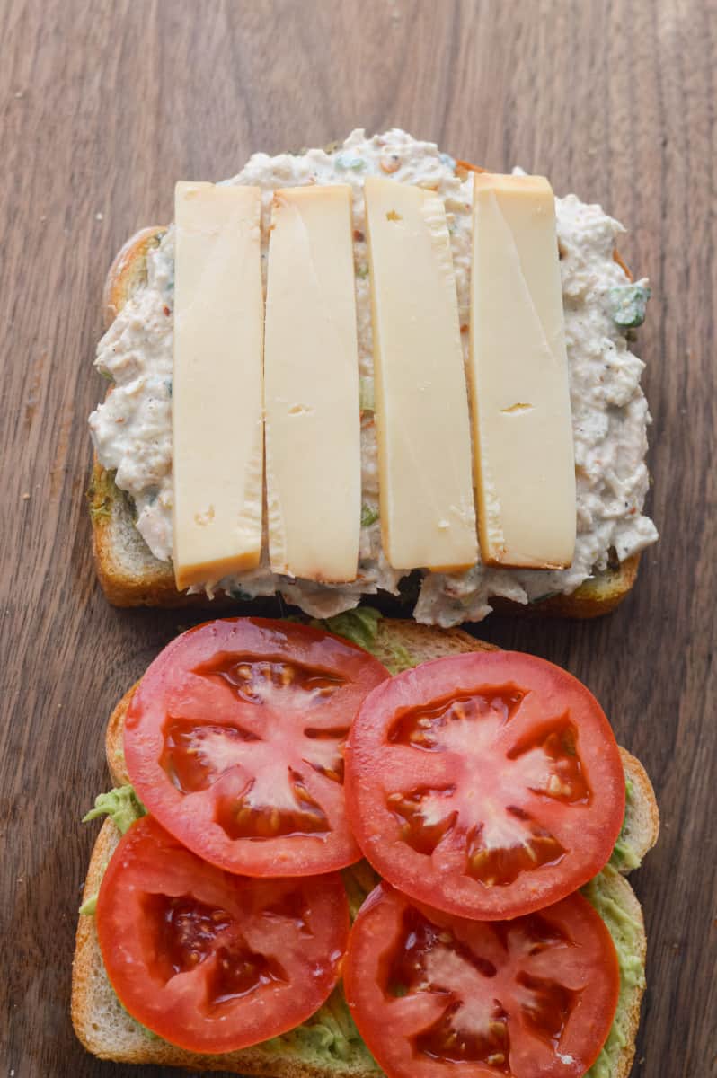 Layering tomato, cheese and tuna salad onto sandwich.