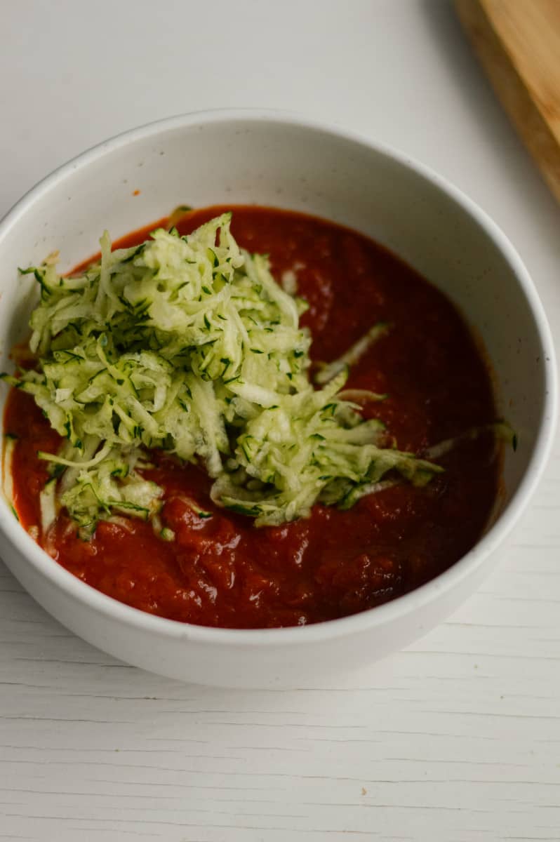 Mixing shredded zucchini with tomato sauce.