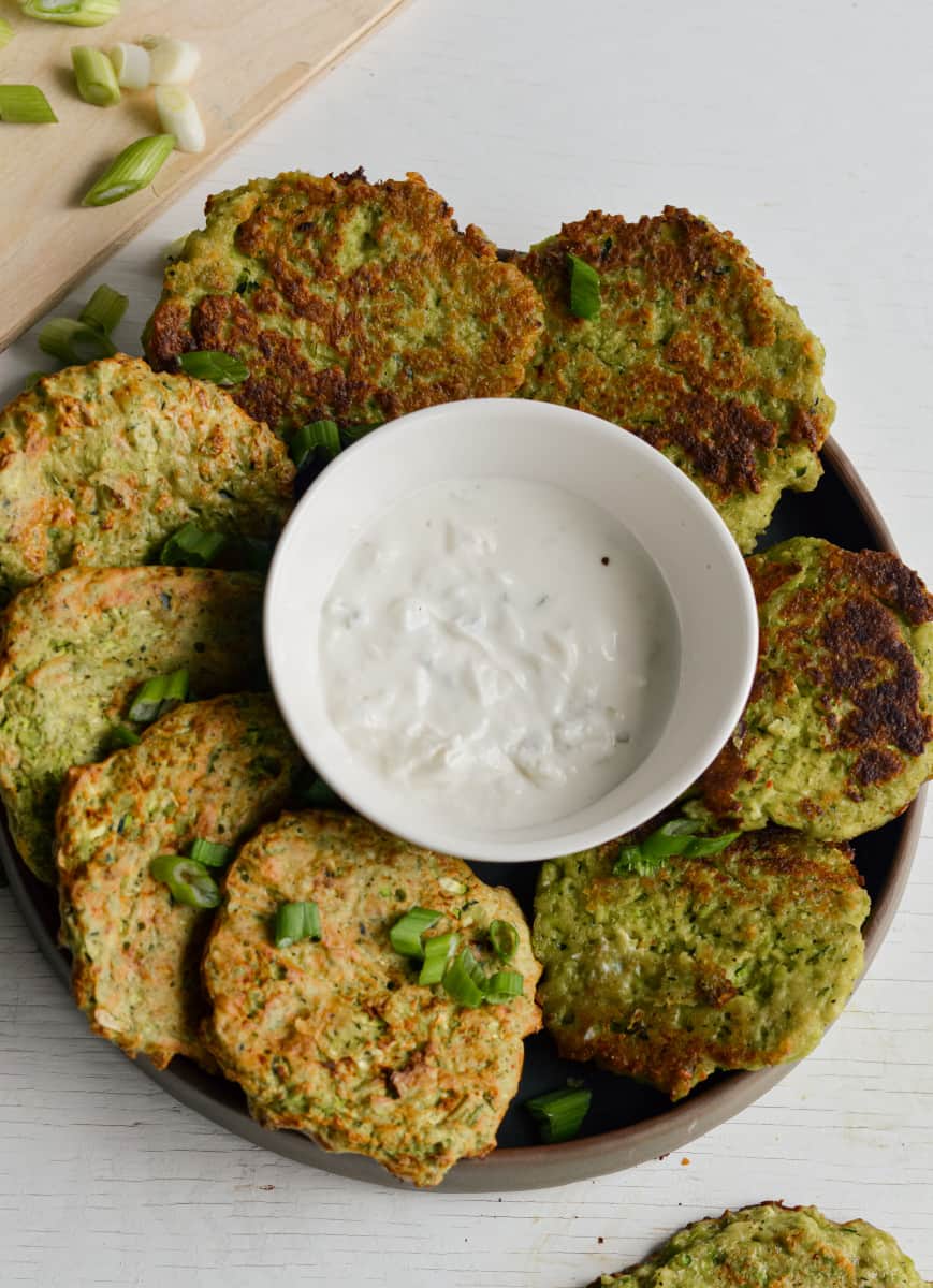 Serving zucchini and edamame fritters on a plate with dip.