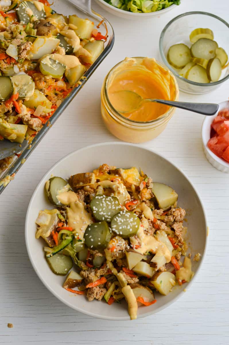 Serving big mac casserole in a bowl with sauce and pickles.