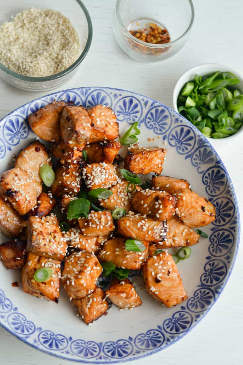 Topping air fryer teriyaki salmon with sesame seeds and green onions.