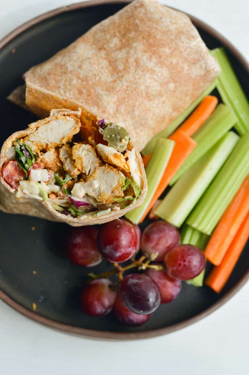 Honey mustard chicken wrap served with veggies and grapes.