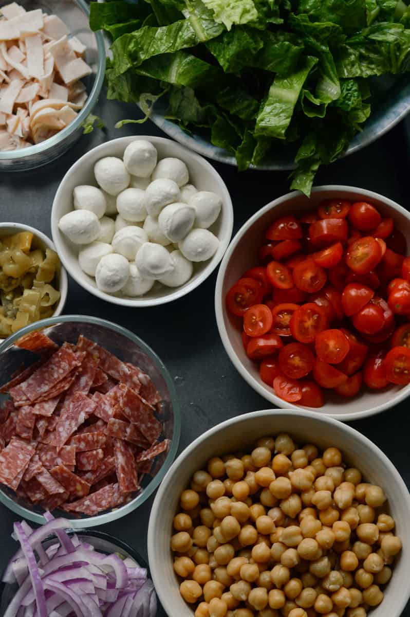 Ingredients for antipasto salad including bocconcini, deli meat, and veggies.