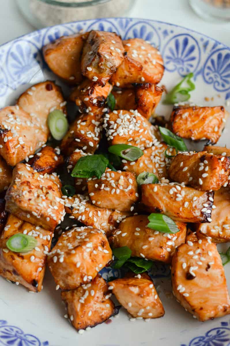 Plate of air fryer teriyaki salmon bites with green onions and sesame seeds.