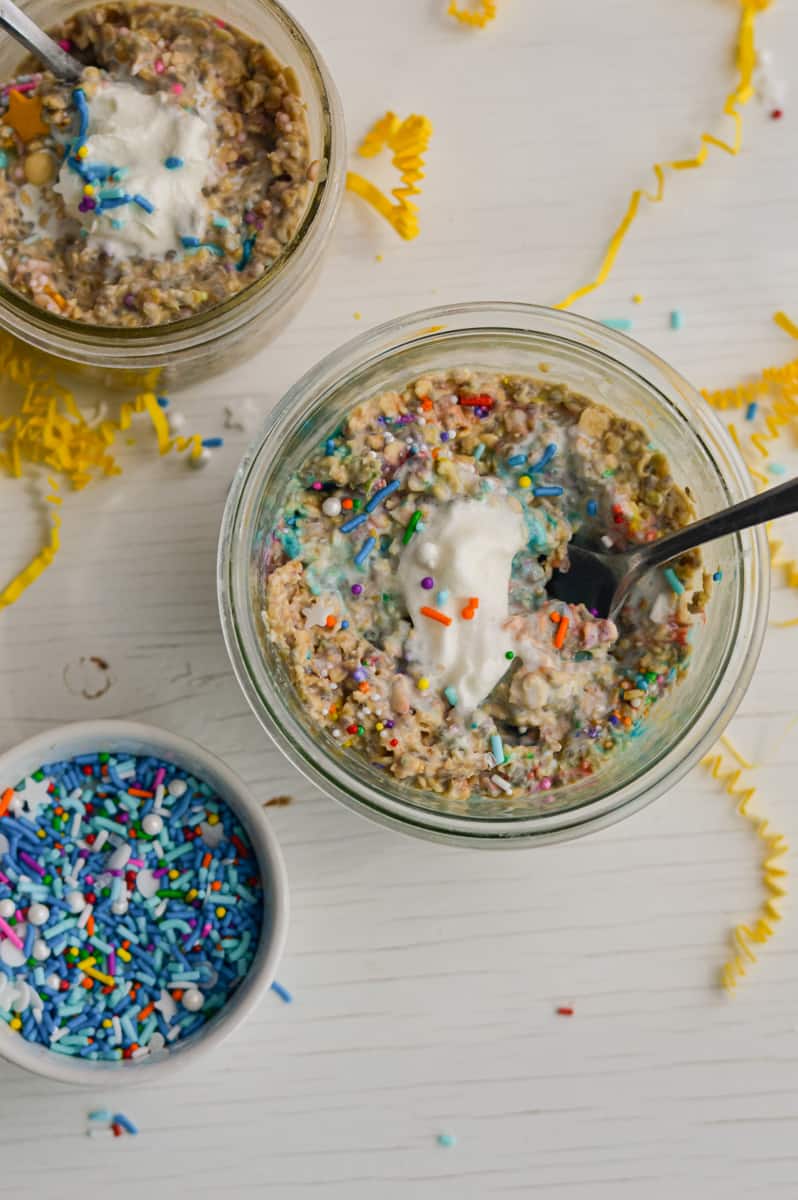 Adding sprinkles and whipped cream to birthday cake overnight oats.