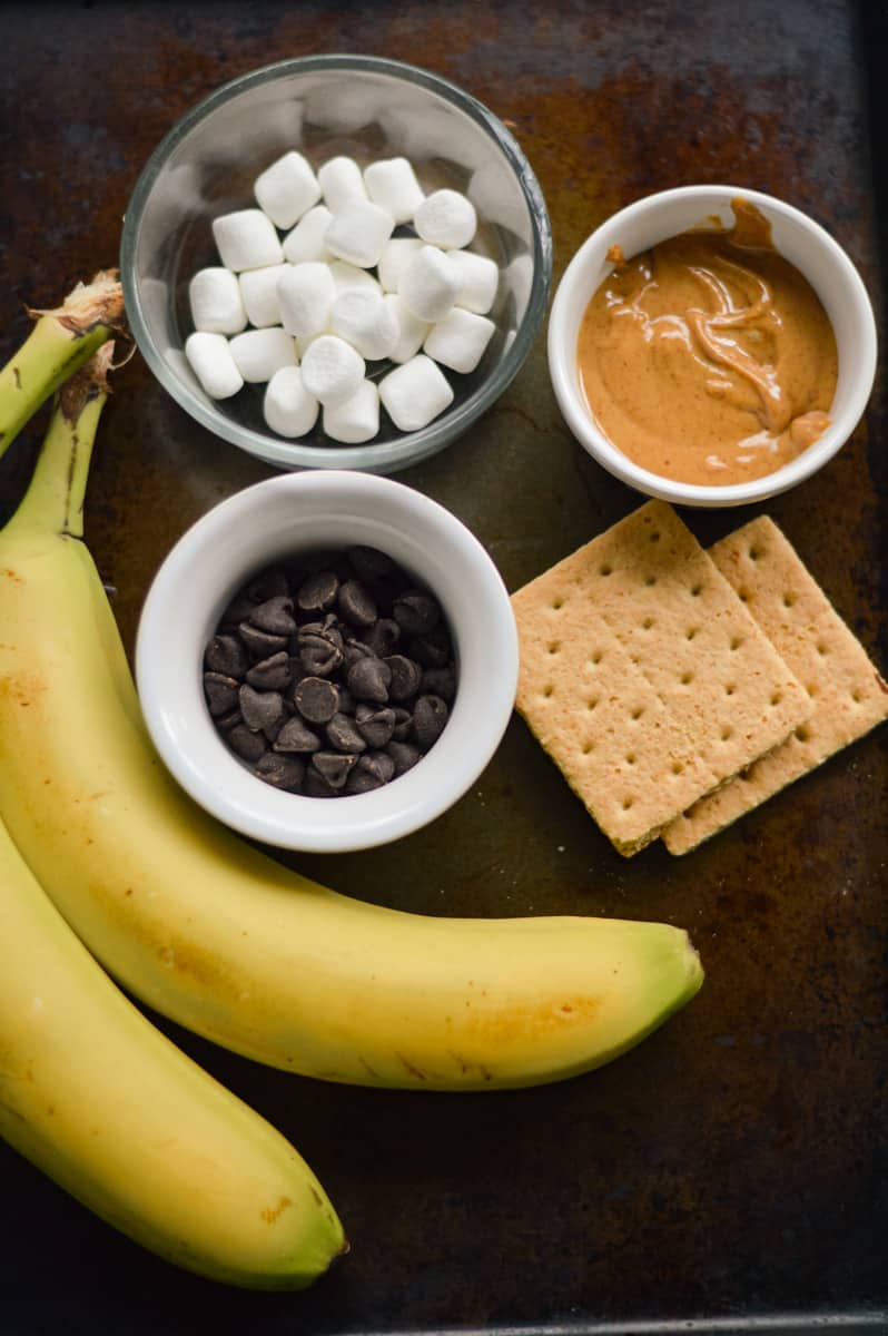 Ingredients for air fried banana split including bananas, chocolate chips, marshmallows, peanut butter and graham crackers.