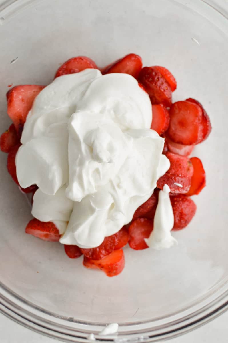 Adding yogurt to strawberries in a bowl.