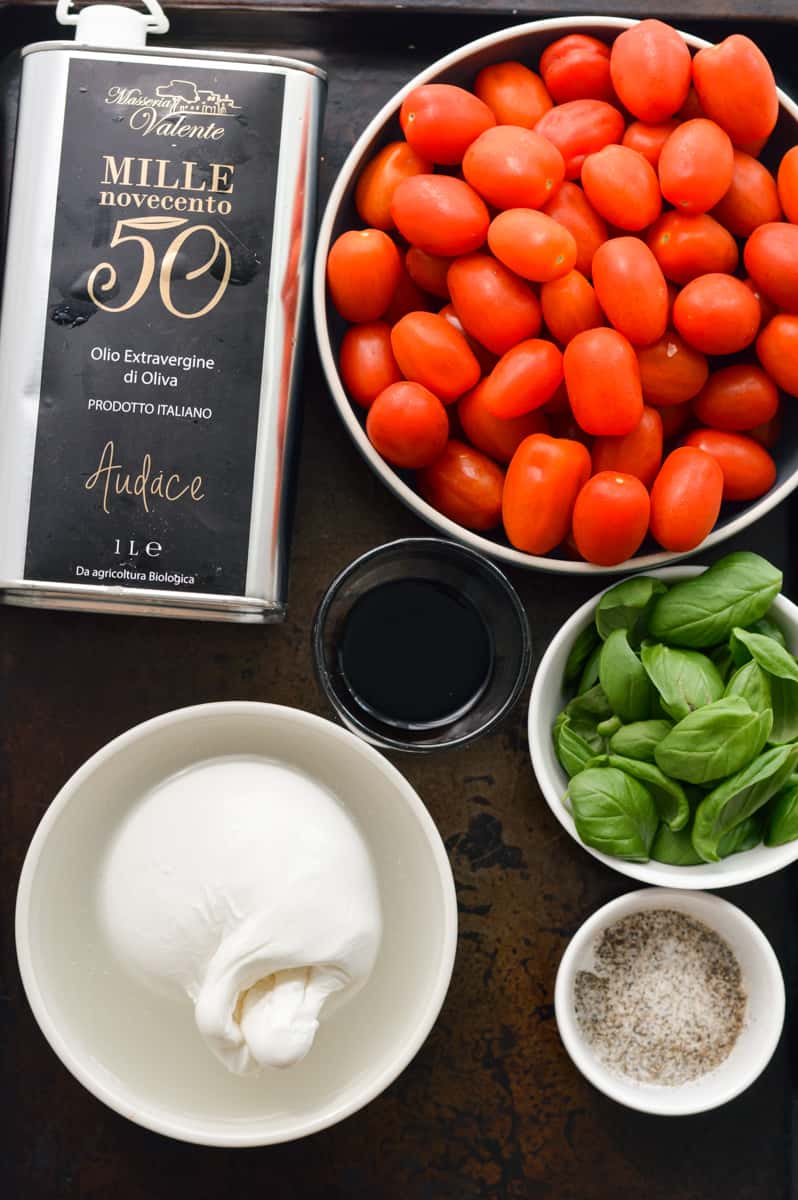 Ingredients for caprese salad including olive oil, balsamic, basil, tomatoes, and burrata.