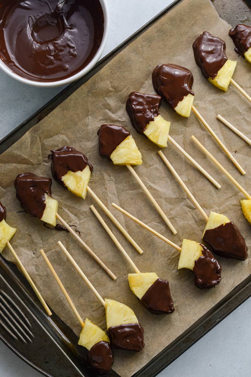 Dipping pineapple pieces in melted chocolate.