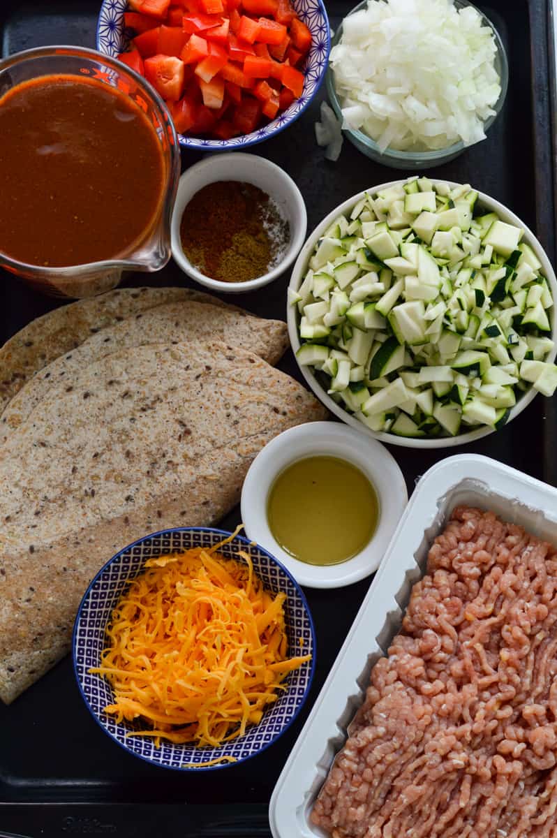 Ingredients including tortillas, ground chicken, cheese, veggies, and enchilada sauce.