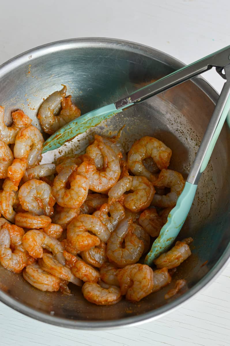 Mixing shrimp in spices in a bowl with tongs.
