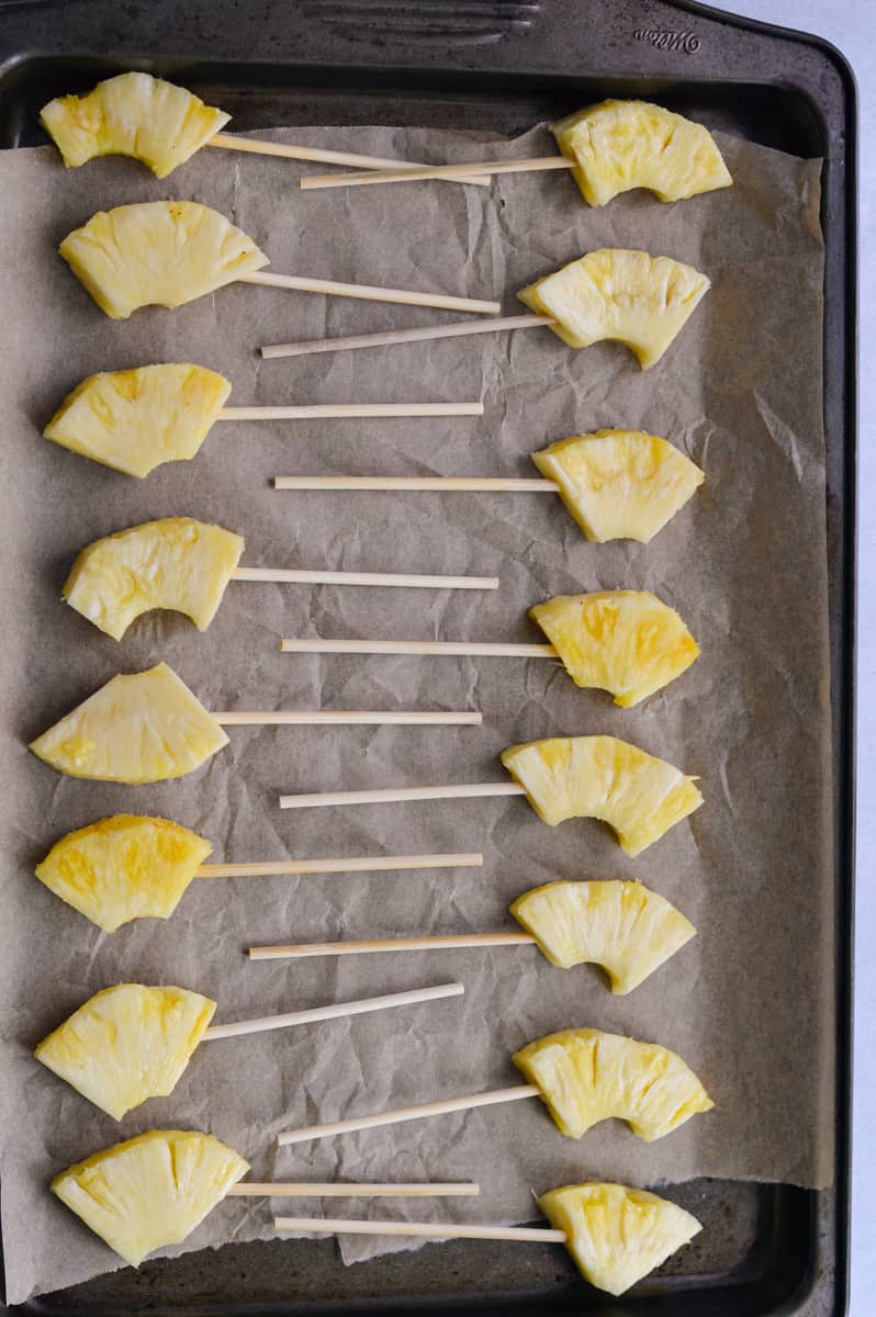 Skewered pineapples on a baking sheet.