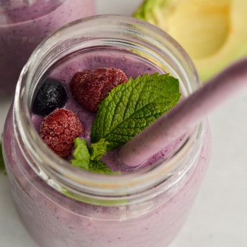 Berry high fiber smoothie with a straw, mint leaves and fresh berries.
