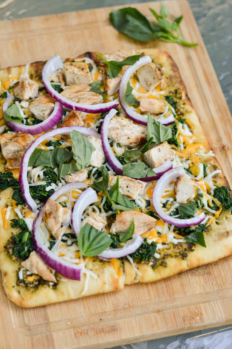 Topping chicken pesto flatbread with fresh basil.