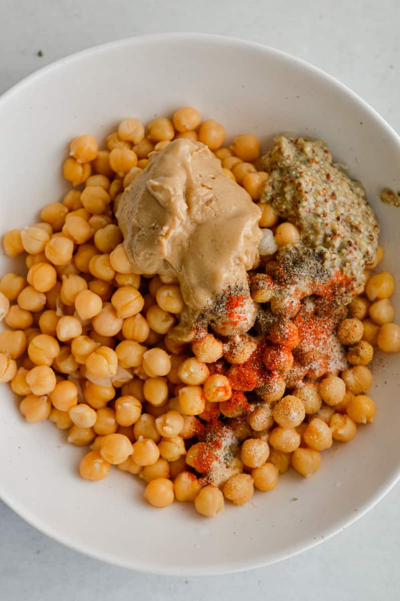 Adding tahini, chickpeas, and spices into a bowl.
