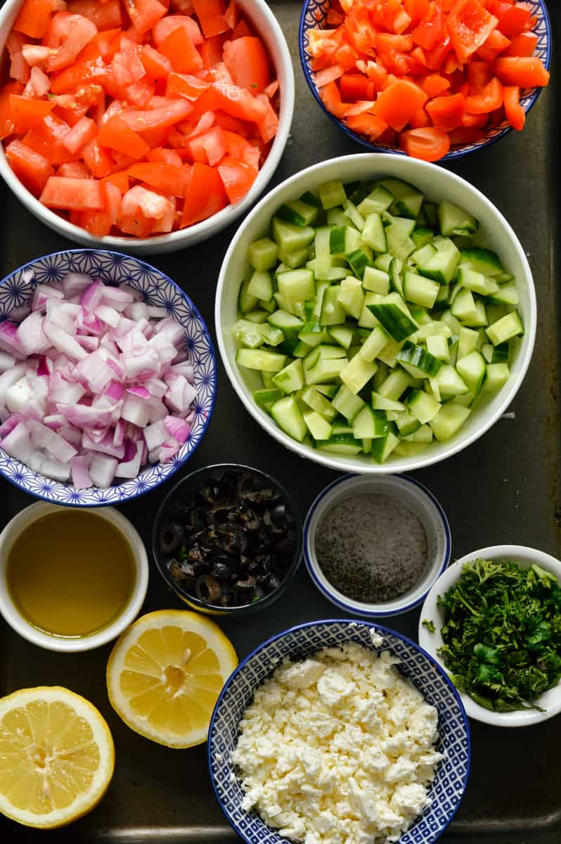 Ingredients including chopped tomatoes, cucumbers, red onions, lemon, parsley, feta and olives.