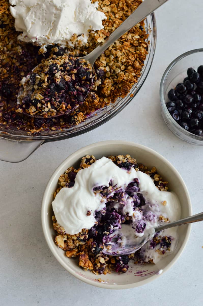 Serving a bowl of blueberry crisp, topped with whipped cream.