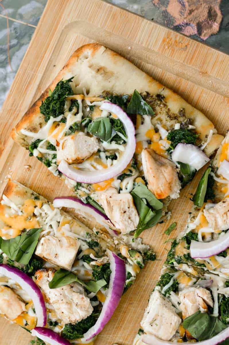 Slices of chicken pesto flatbread with red onion and spinach.