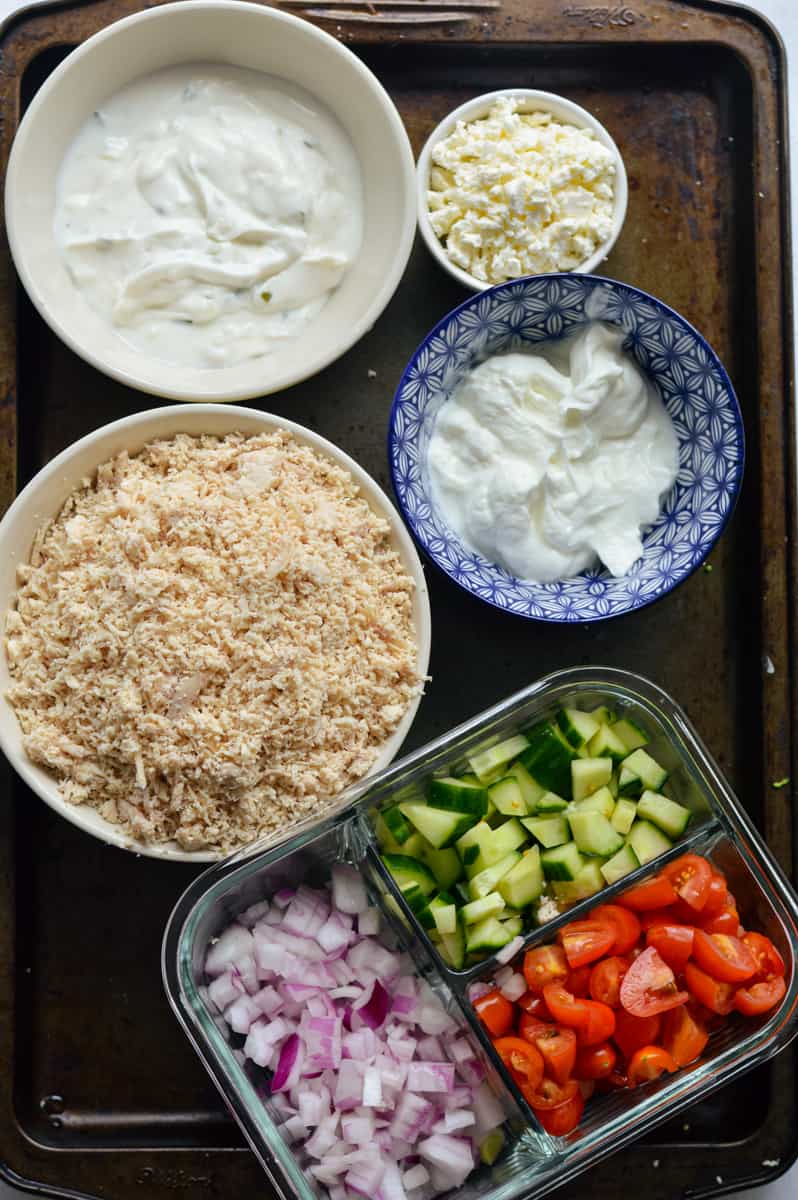 Ingredients including shredded chicken, tzatziki, cherry tomatoes, red onions, cucumbers, Greek yogurt and mayo.