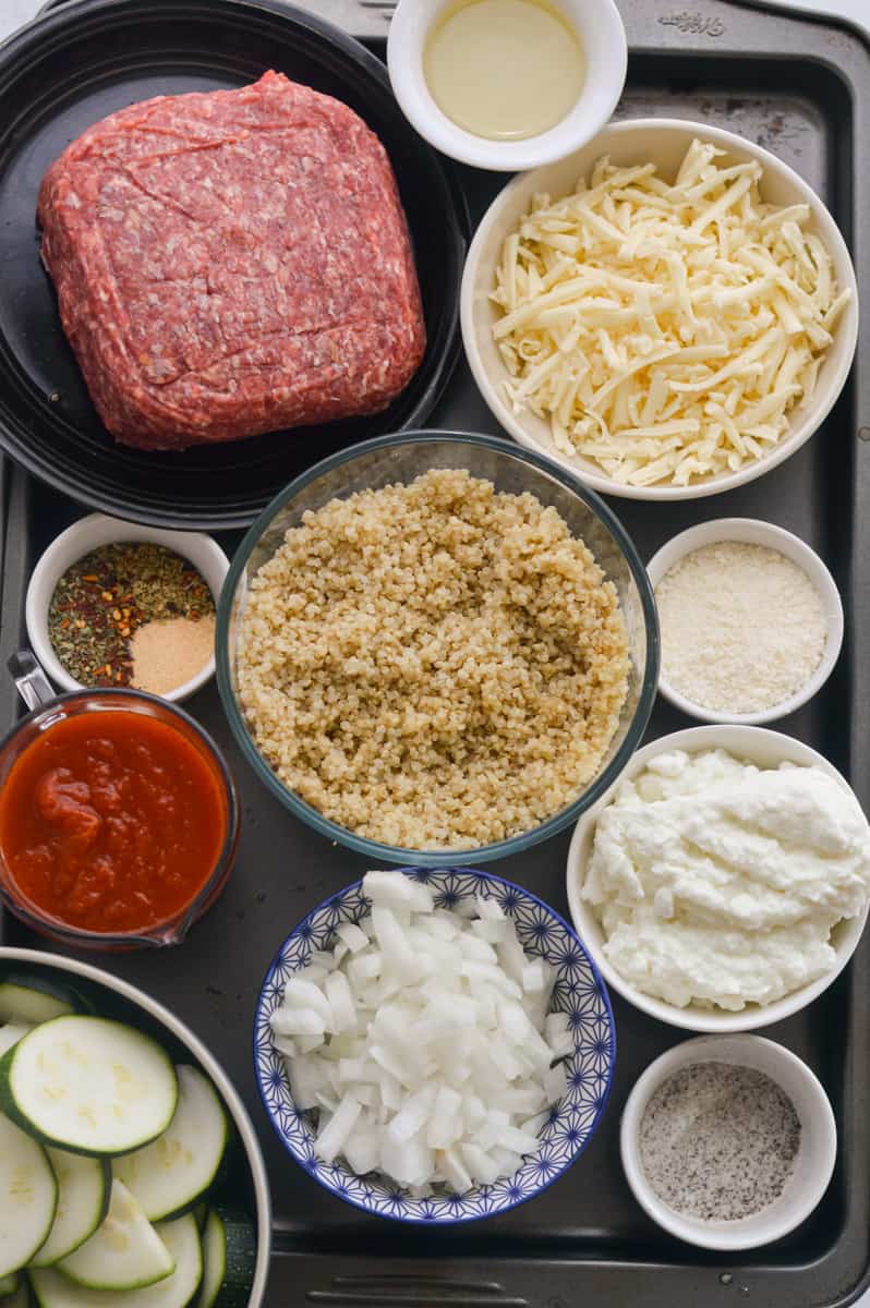 Ingredients including ground beef, mozzarella, cottage cheese, zucchini, quinoa, tomato sauce and seasoning.