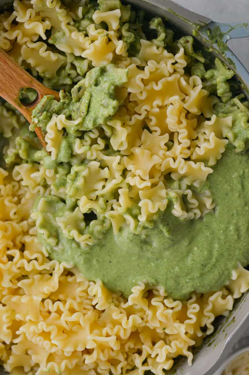 Adding green pasta sauce to cooked pasta.