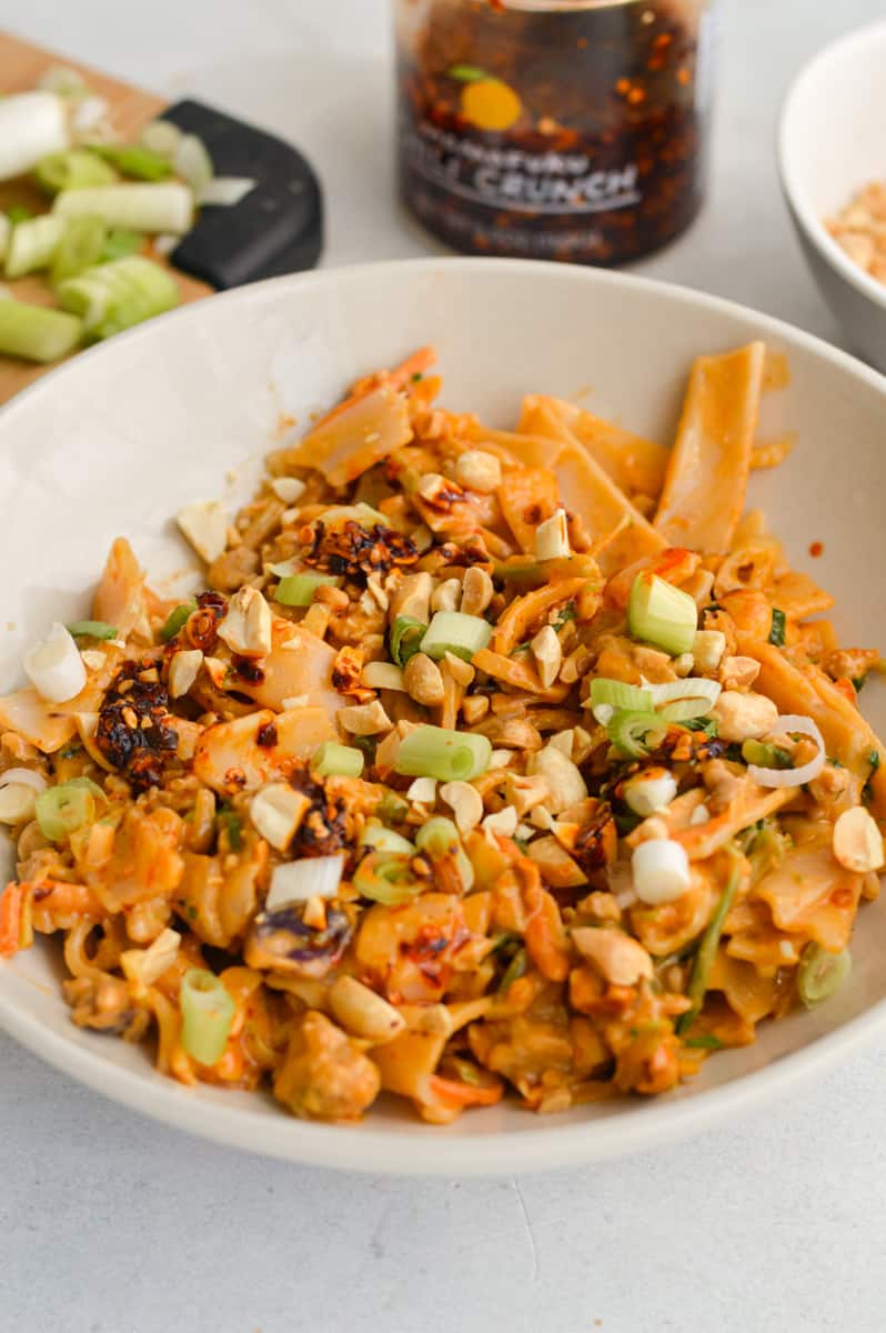 Serving spicy peanut noodles in a bowl with chili crunch, green onion and chopped peanuts.