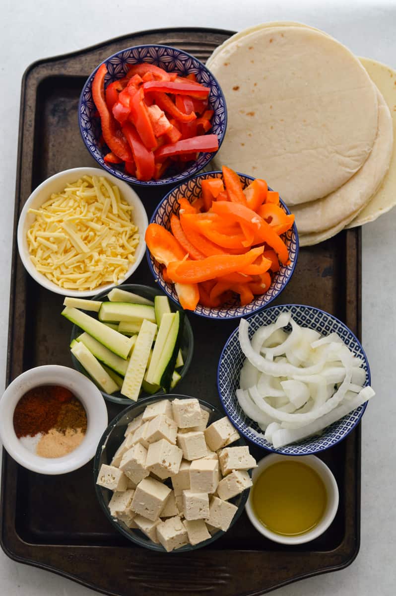 Ingredients including bell peppers, zucchini, dairy-free cheese, tortillas, tofu, onion and fajita seasoning.