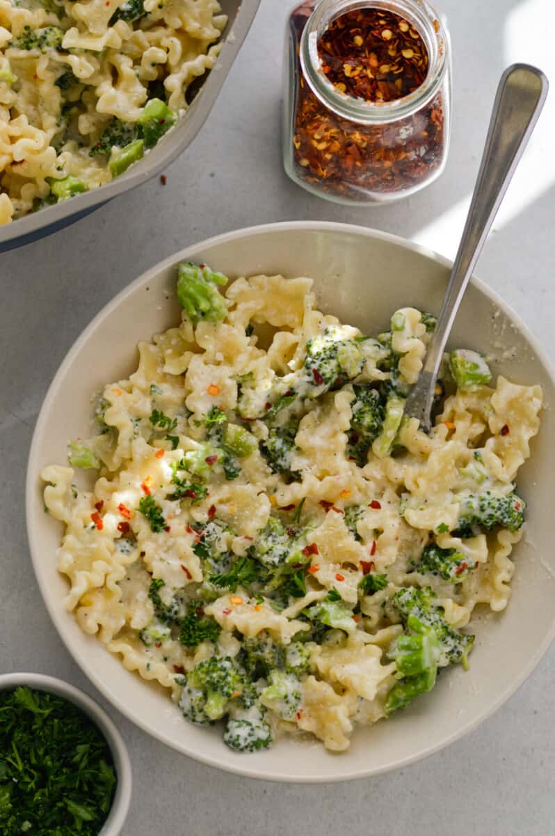Bowl of cottage cheese alfredo pasta with broccoli and red pepper flakes.