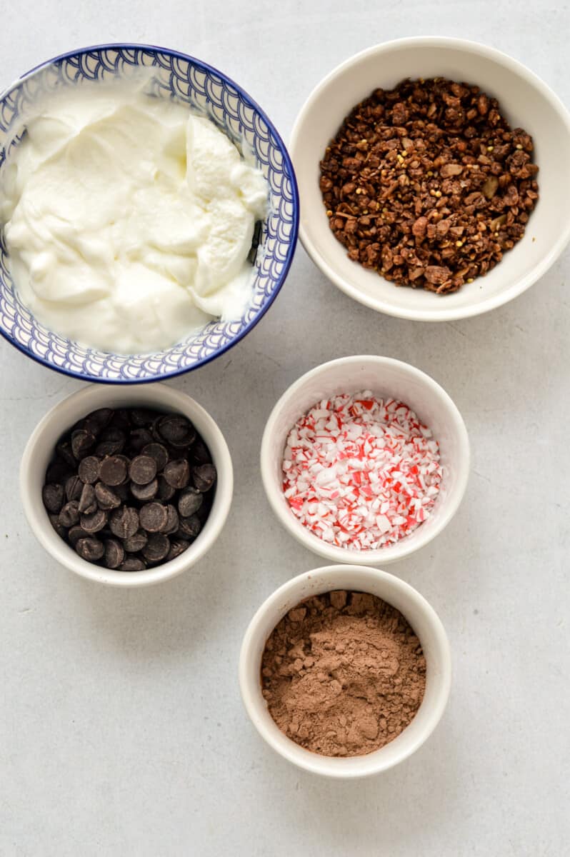 Ingredients including Greek yogurt, chocolate protein powder, crushed candy cane, chocolate chips, cocoa powder, granola.