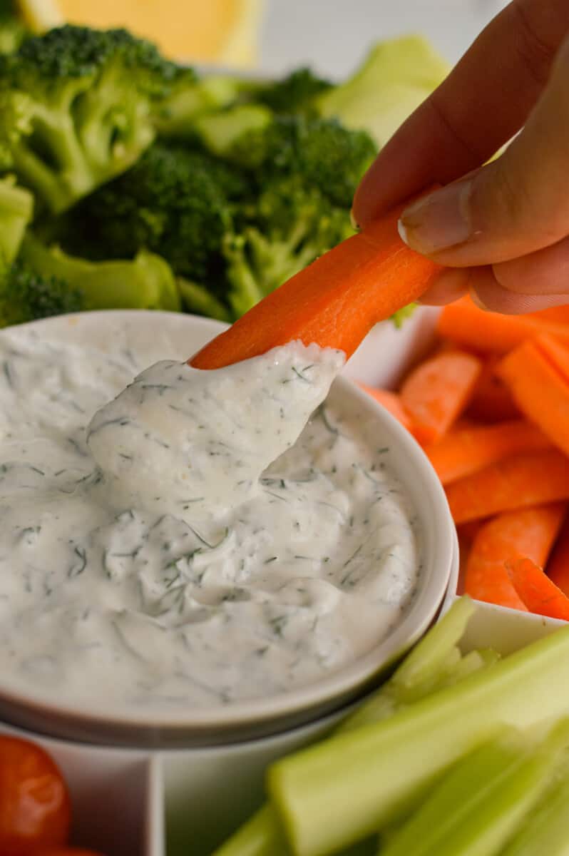 Dunking a baby carrot into Greek yogurt dill veggie dip.