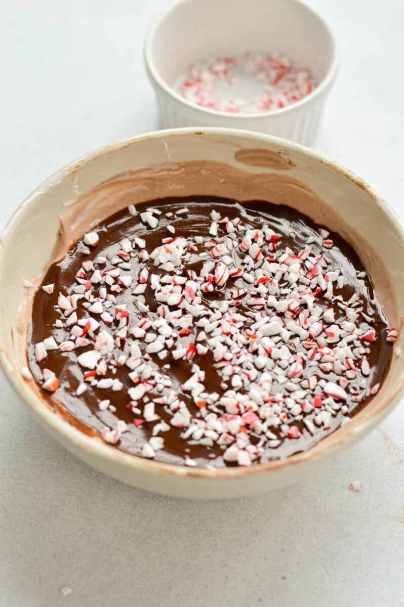 Sprinkling crushed candy canes on chocolate magic shell yogurt bowl.