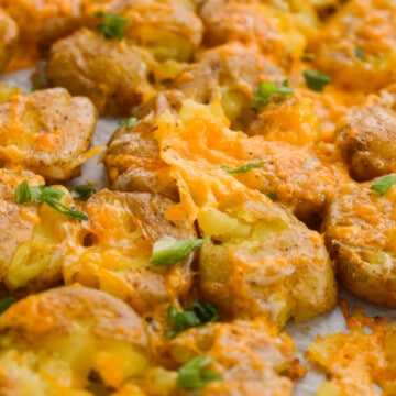 Close up of cheesy smashed potatoes topped with chives.