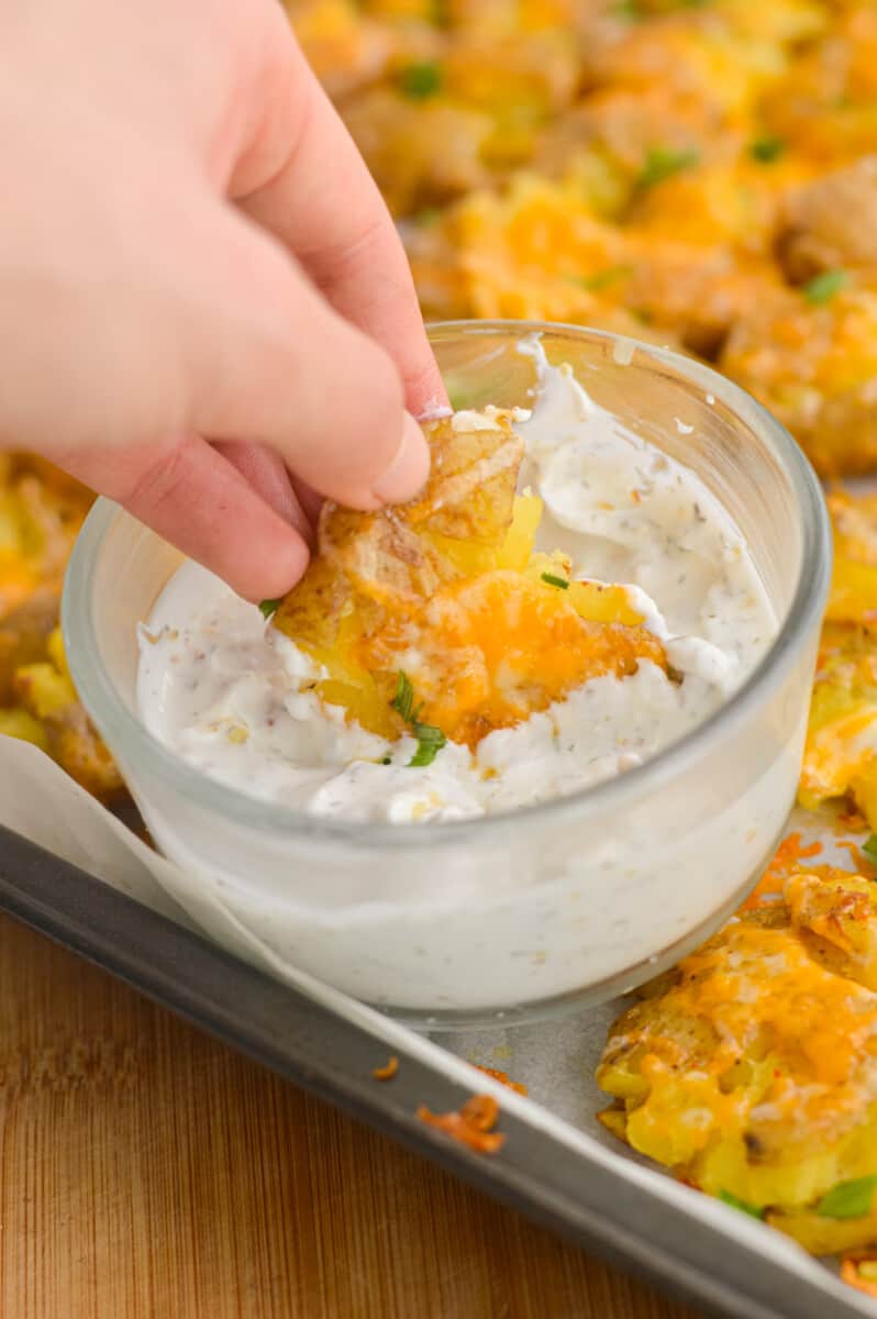 Dipping cheesy smashed potatoes in white dip.