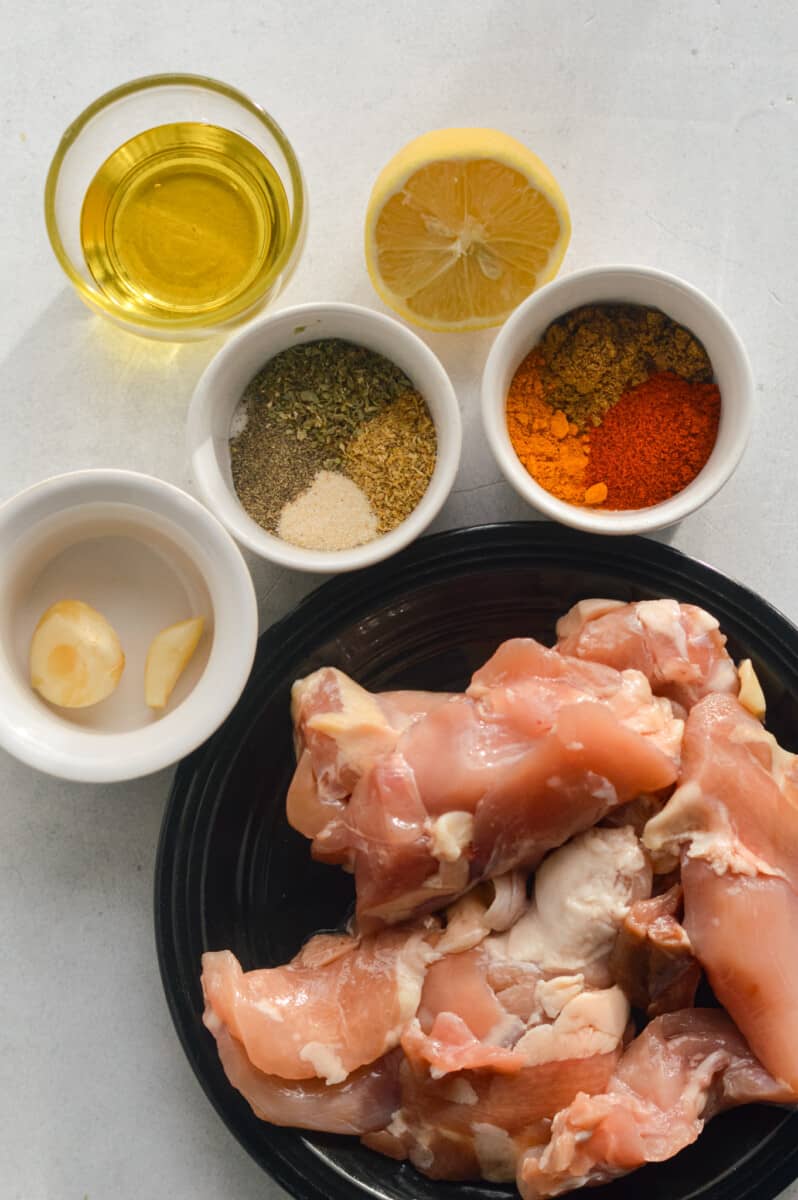Ingredients including chicken thighs, garlic, spices, olive oil and lemon.