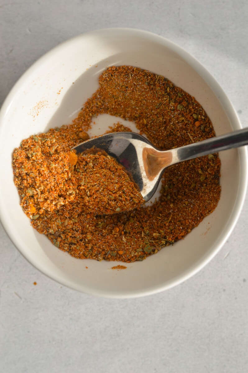 Mixing cumin, paprika, turmeric, salt, black pepper, coriander, onion powder, and oregano in a bowl.
