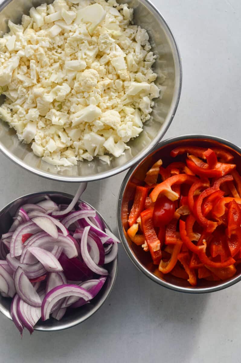 Ingredients including red bell peppers, cauliflower and red onion.