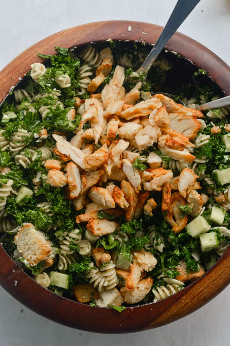 Adding thin sliced chicken breast to kale Caesar pasta salad.