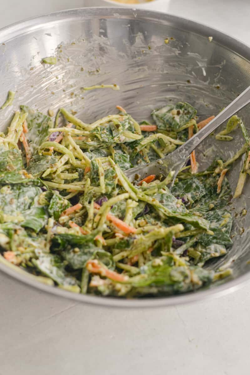 Mixing spinach and coleslaw with Greek yogurt and pesto.