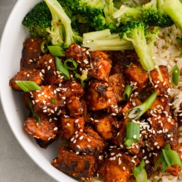 Close up of sticky orange tofu in a bowl with brown rice and broccoli.