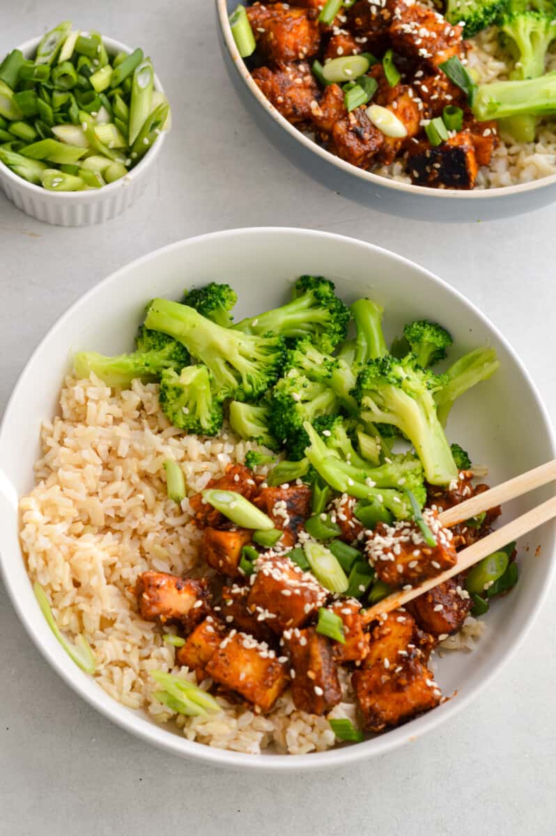 Birds eye of bowl with sticky orange tofu, broccoli, brown rice and chopsticks.
